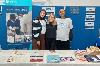 Three students smiling behind stand at dental school event